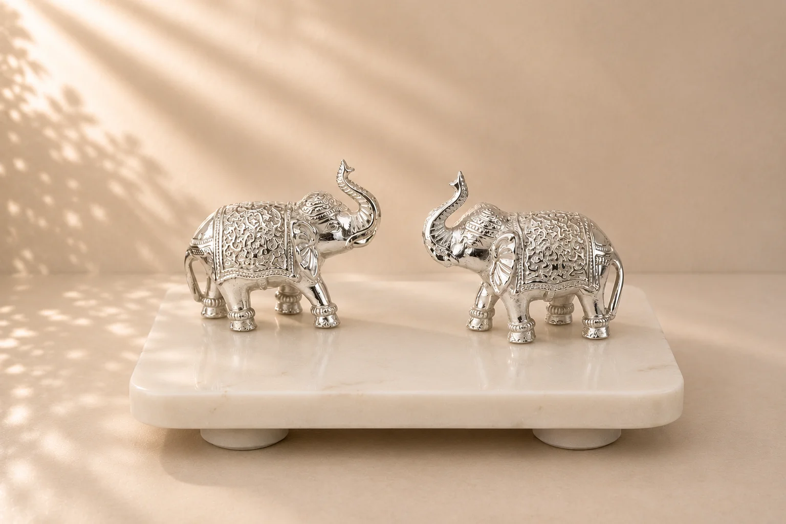 A pair of silver-plated elephants with hand-embossed detailing, on a marble plinth